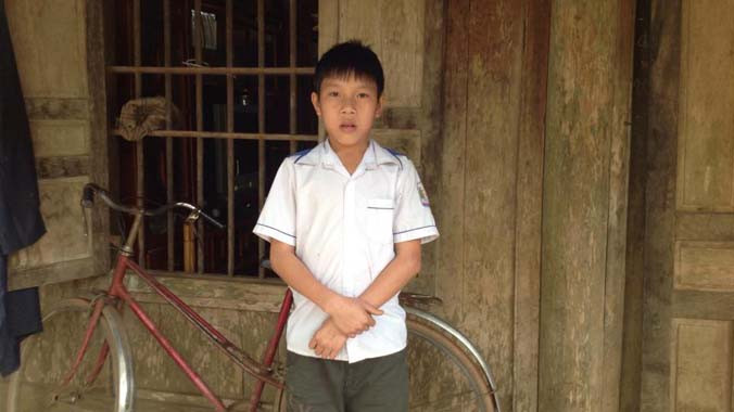 Em Tuấn trước căn nhà gỗ đơn sơ của gia đình.