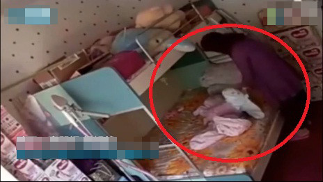 Bảo mẫu dùng khăn trùm kín đầu em bé 7 tháng tuổi. Ảnh cắt từ clip