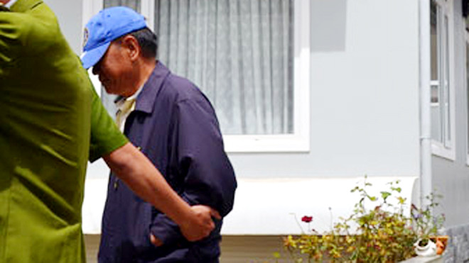 Ông Ngọ (áo xanh) bị áp giải ra khỏi nhà