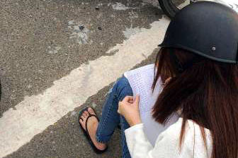 Nữ sinh viên ngồi chép phạt 50 lần sau khi vi phạm lỗi đi ngược chiều. Ảnh: Đào Phan