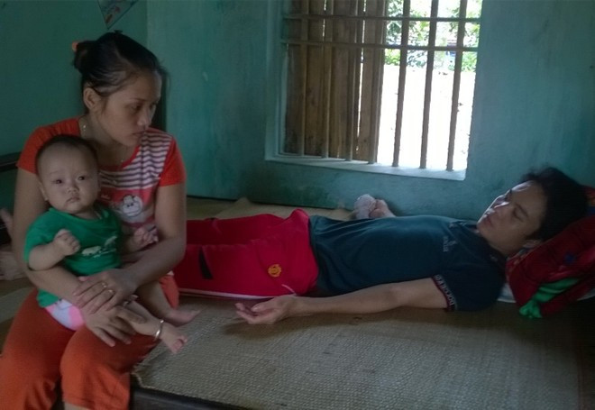 Chị Hiên bế đứa con út ngồi cạnh chồng bị tai nạn dẫn đến mất khả năng lao động