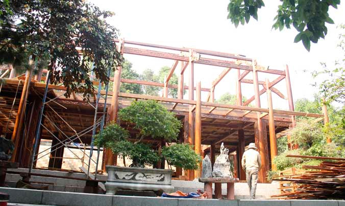 Ngôi nhà gỗ đã được tháo dỡ xong phần mái, các công nhân đang dỡ các cột, kèo.