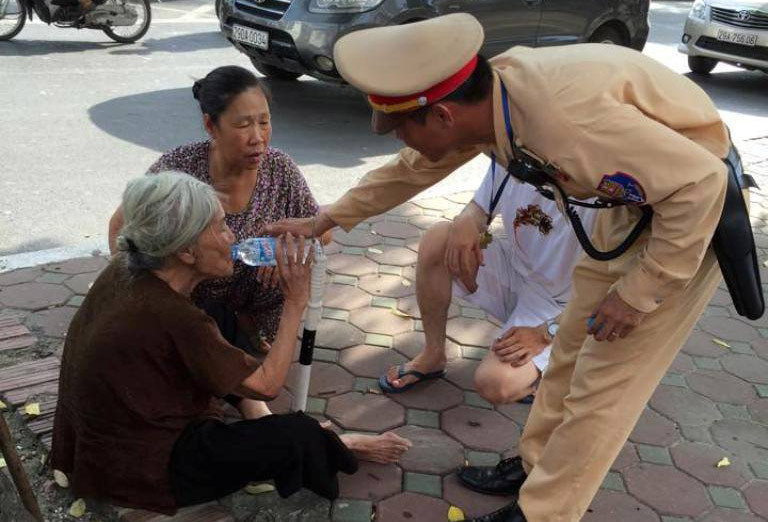 Cụ già được chiến sĩ CSGT dìu vào gốc cây sau khi bị say nắng trên đường.