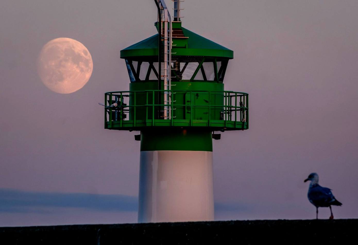 Mặt trăng được nhìn thấy phía sau ngọn hải đăng tại bến cảng Travemünde, Đức. Ảnh: Michael Probst/AP