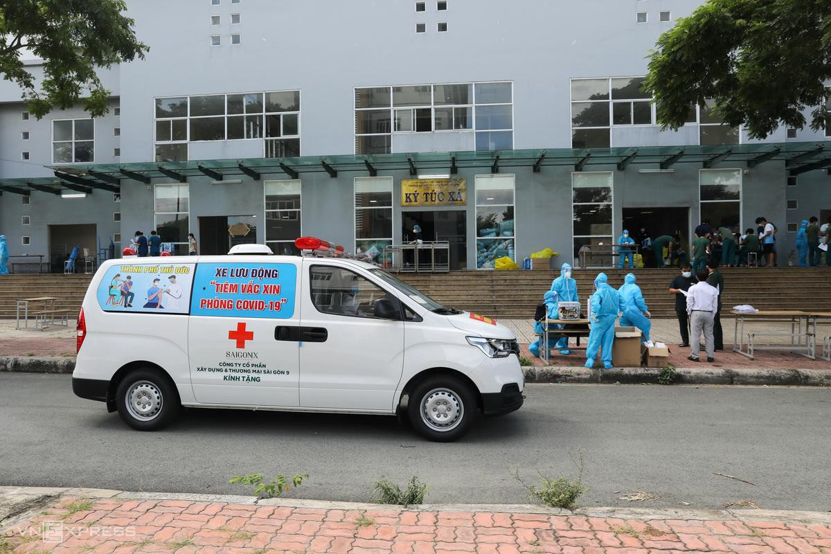 8h30, xe đến điểm tiêm là khu cách ly trong ký túc xá Đại học Văn Hóa (phường Phước Long A), cách Bệnh viện Lê Văn Thịnh 10 km. Vừa xuống xe, nhân viên y tế nhanh chóng mặc đồ bảo hộ trước khi làm nhiệm vụ.