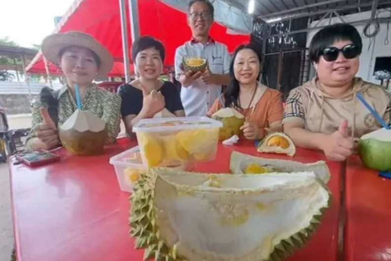 Khách du lịch Trung Quốc ăn sầu riêng tại một quầy trái cây ở Melaka. Ảnh: The Star.