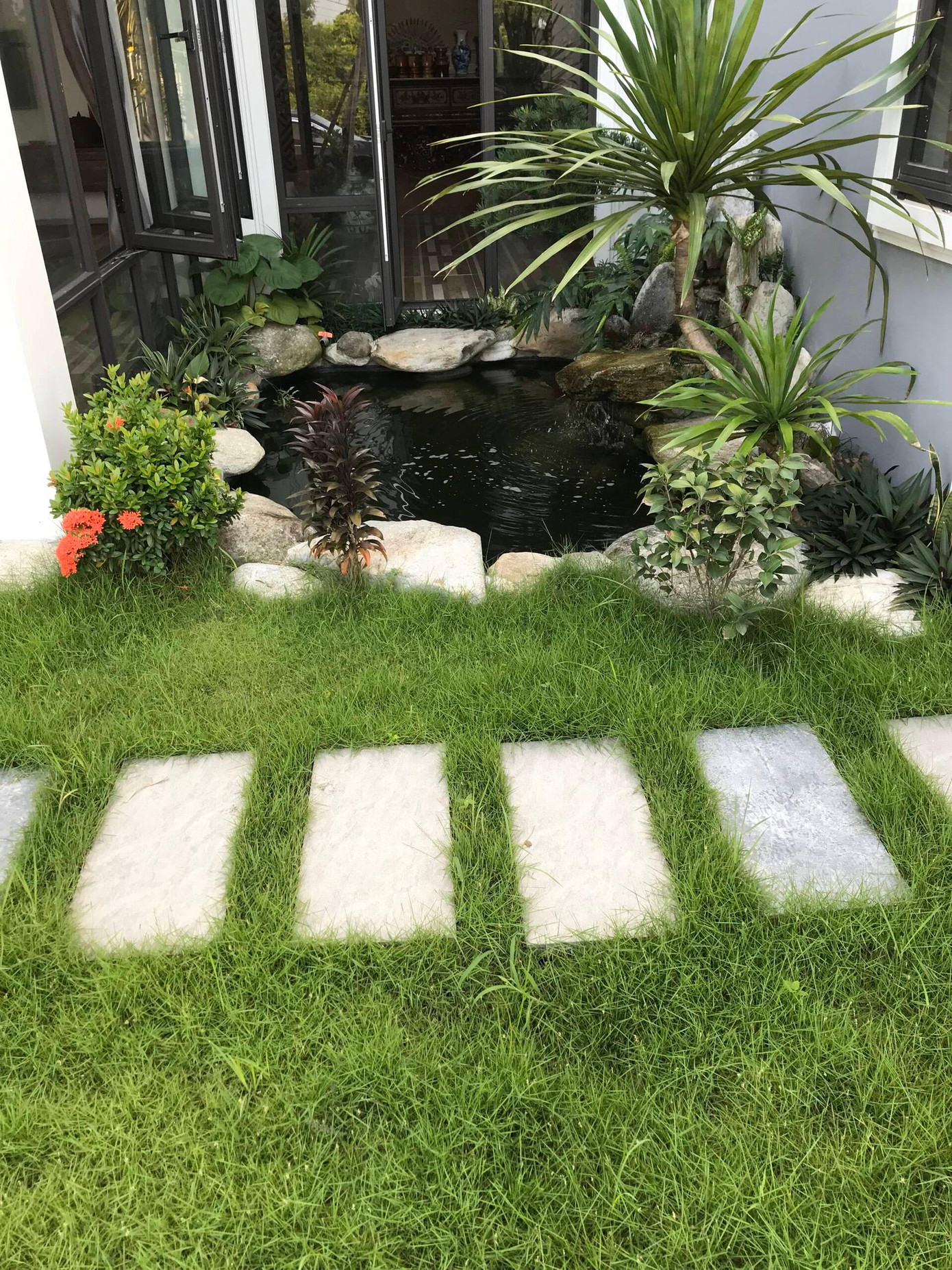 Do biệt thự có mặt tiền quay về hướng Tây Nam rất nóng nên người con chọn giải pháp đẩy sảnh lui vào trong, bố trí hồ nước điều hòa và cây xanh để hạ nhiệt cho phòng khách vào những tháng hè.