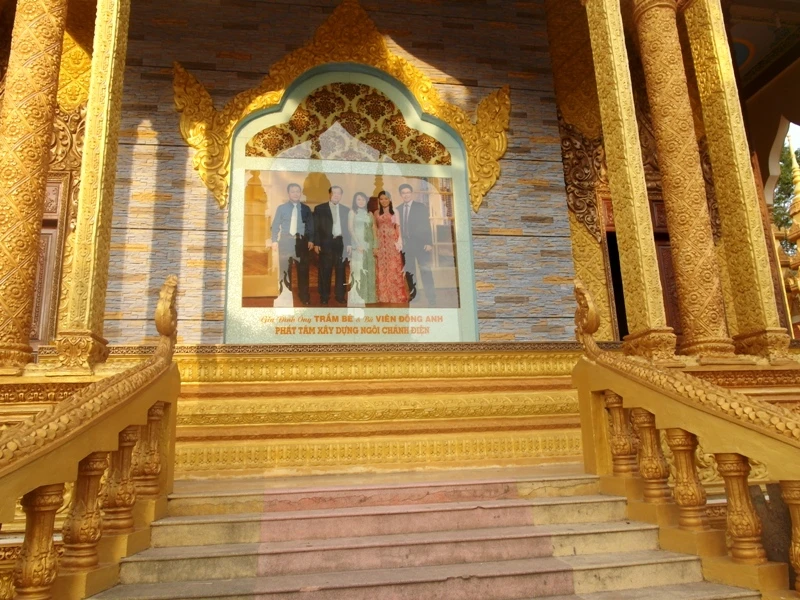 Hình ông Trầm Bê và các thành viên trong gia đình ông bên ngoài vách, lối vào cổng sau ngôi chánh điện chùa Vàm Ray. Một số thông tin sai lệch trên vài tờ báo, cho rằng bức ảnh này được treo... bên trong chánh điện, ngang hàng với tượng Đức Phật Thích Ca Mâu Ni, nghĩa là 