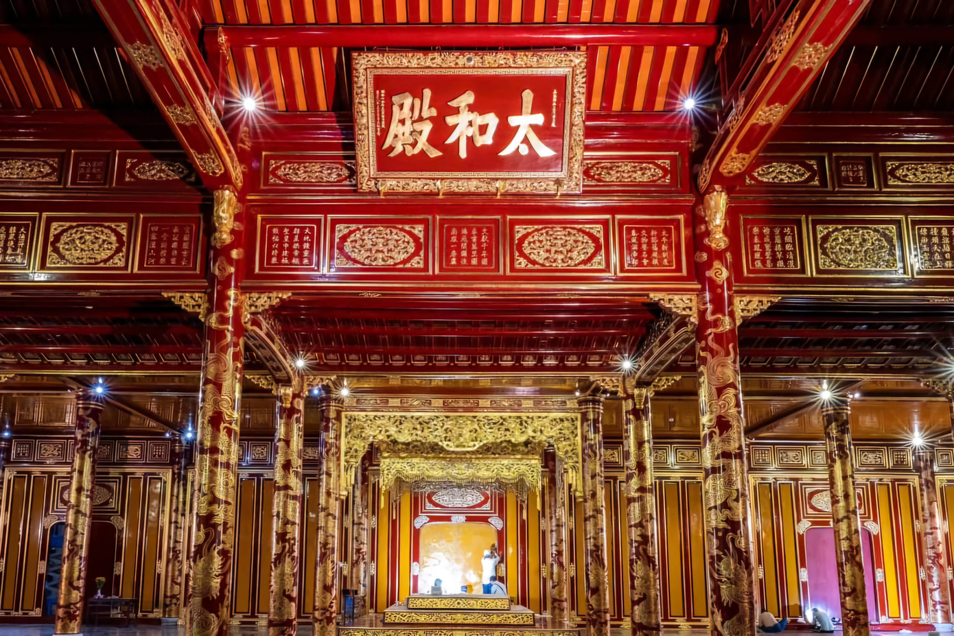 Giữa tiền điện, gần trên mái treo tấm biển sơn son thếp vàng với ba chữ Thái Hòa điện. Phía trong cùng, ở gian giữa chính điện đặt ngai vua ba tầng bệ gỗ, bên trên treo bửu tán bằng pháp lam ngũ sắc trang trí chín con rồng. Ngai và bửu tán đều thếp vàng chói lọi rực rỡ. Ảnh: TTBTDTCĐ.