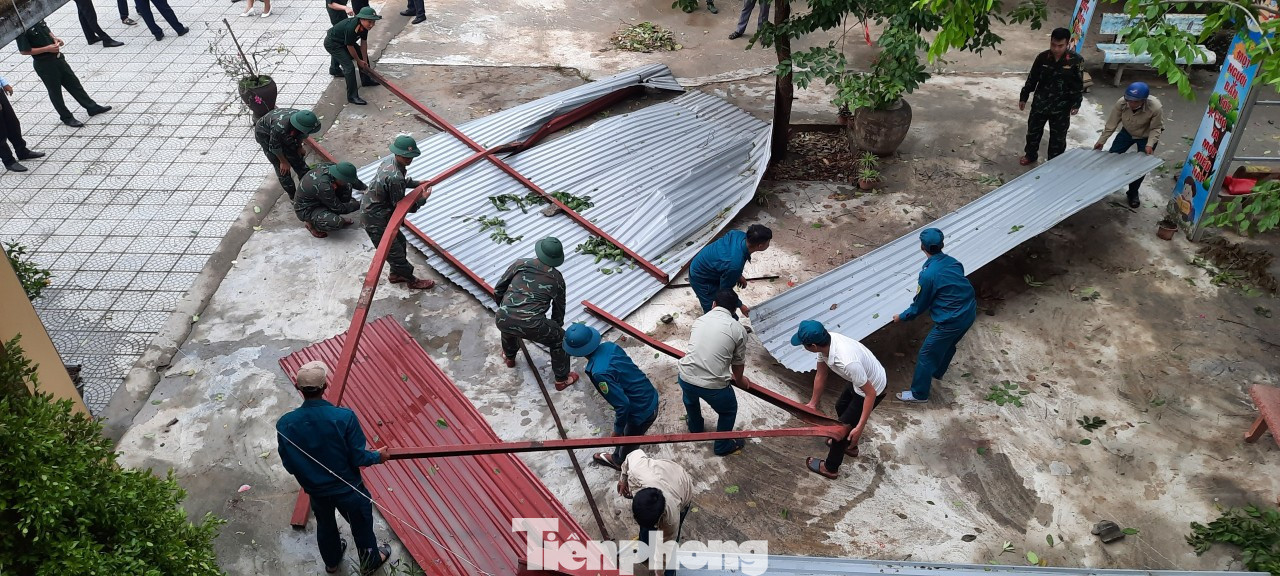 Lực lượng bộ đội, dân quân tự vệ, người dân giúp nhà trường dọn dẹp phần mái bị lốc cuốn bay.