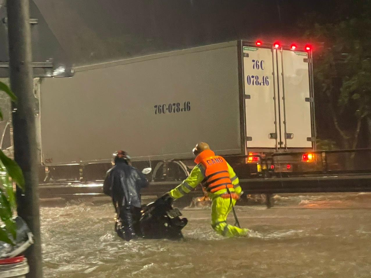 CSGT hỗ trợ đẩy xe máy bị ngừng động cơ do ngập nước qua đoạn đường lũ lụt. Ảnh: CA