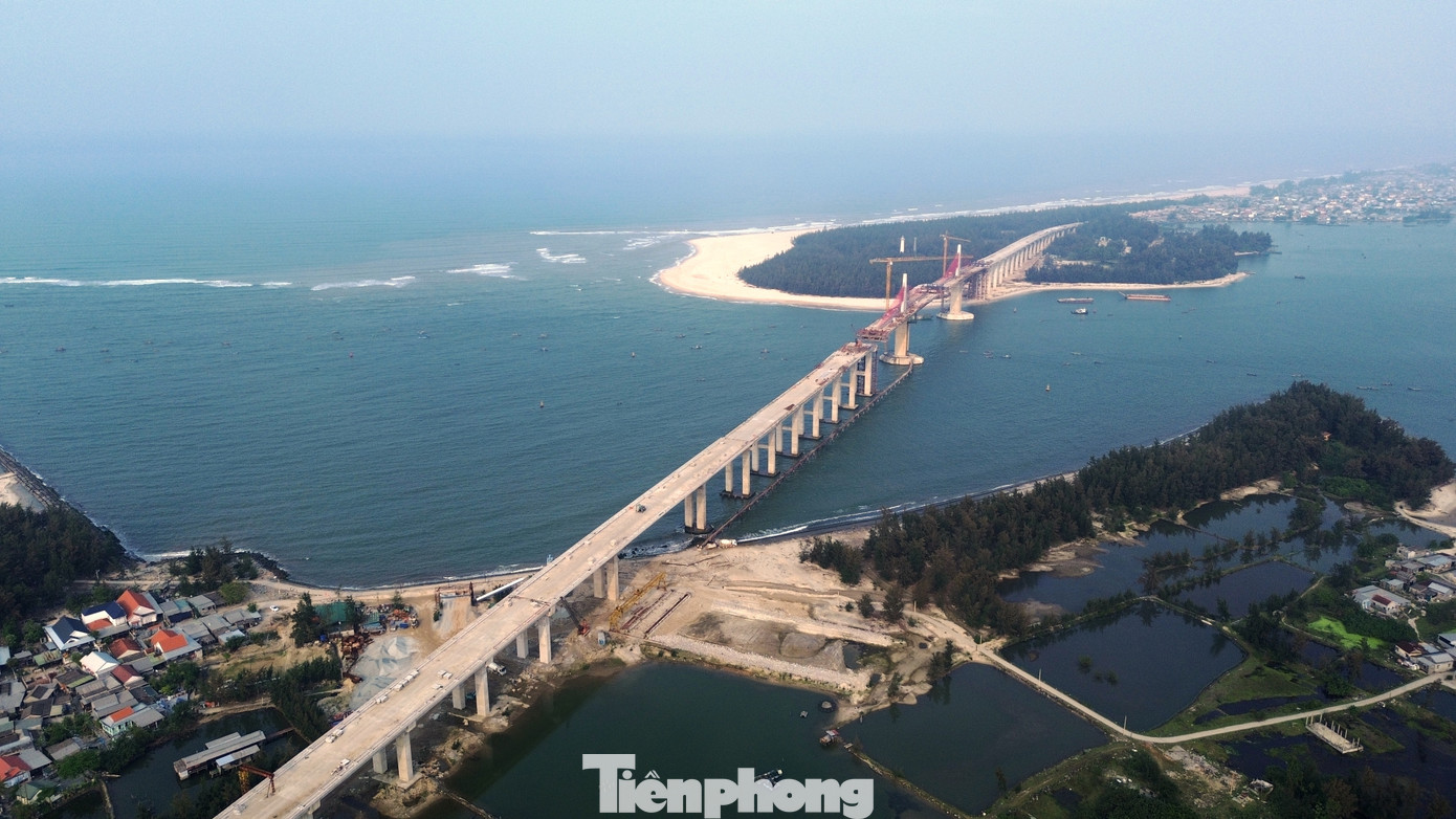 Nhìn từ trên cao, cây cầu như một dải lụa đỏ mềm mại vắt qua cửa biển Thuận An, nổi bật giữa nền trời và mặt biển xanh.