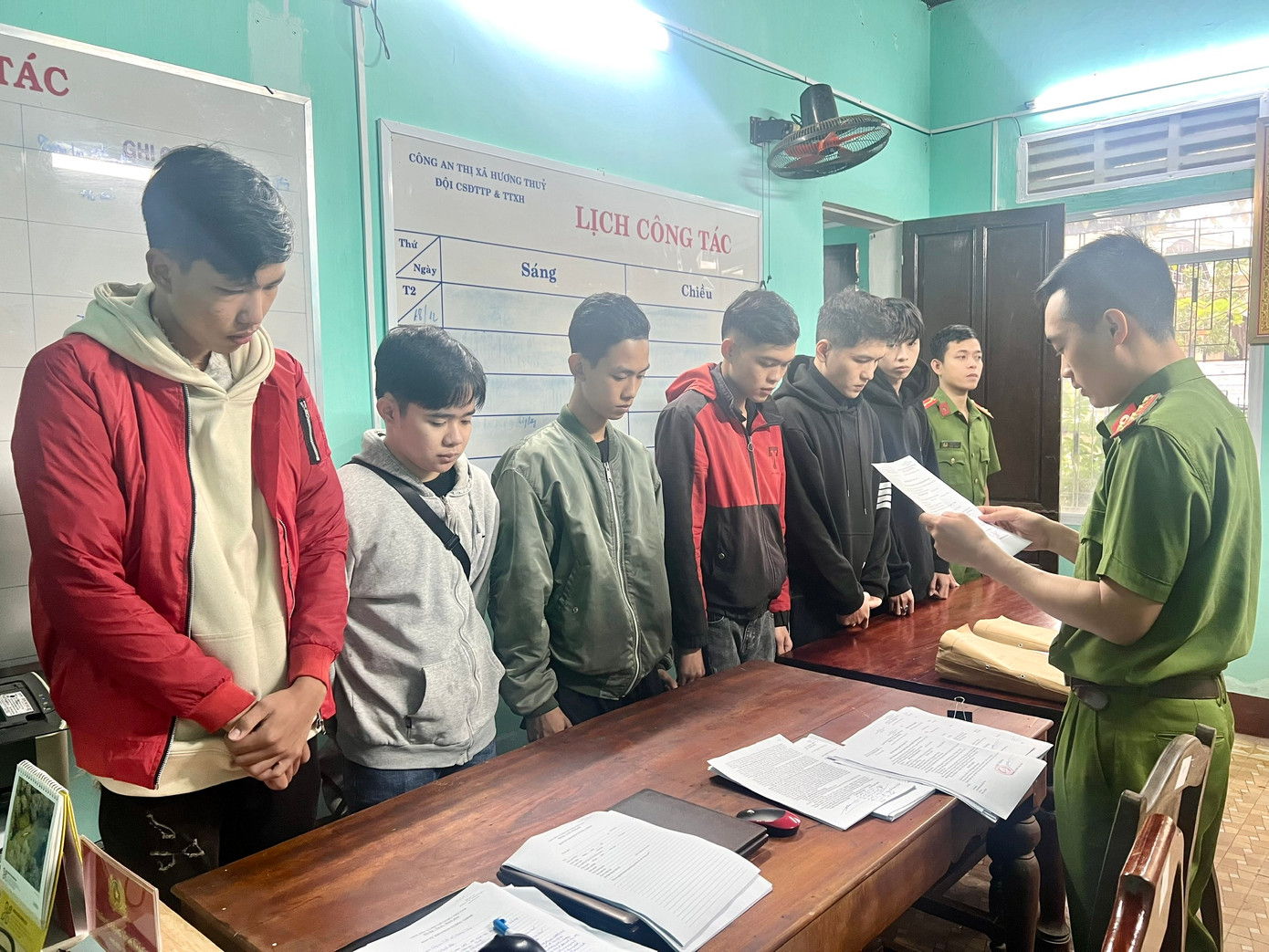 Đọc lệnh khởi tố Đinh Sơn Nhật Tiến (áo đỏ, bìa trái) cùng 12 đối tượng liên quan về hành vi tổ chức đua xe trái phép và gây rối trật tự công cộng. (Ảnh: CACC)