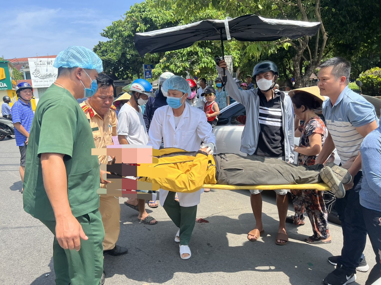 Hai cán bộ công an phối hợp với người dân và các nhân viên y tế đưa shipper gặp nạn đi cấp cứu. Ảnh: CACC