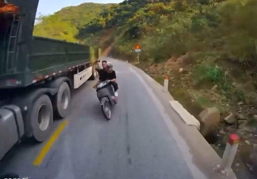Hai thanh niên đi xe máy cố tình vượt lên xe đầu kéo chở quặng và đối đầu với xe bồn lưu thông theo hướng ngược lại.