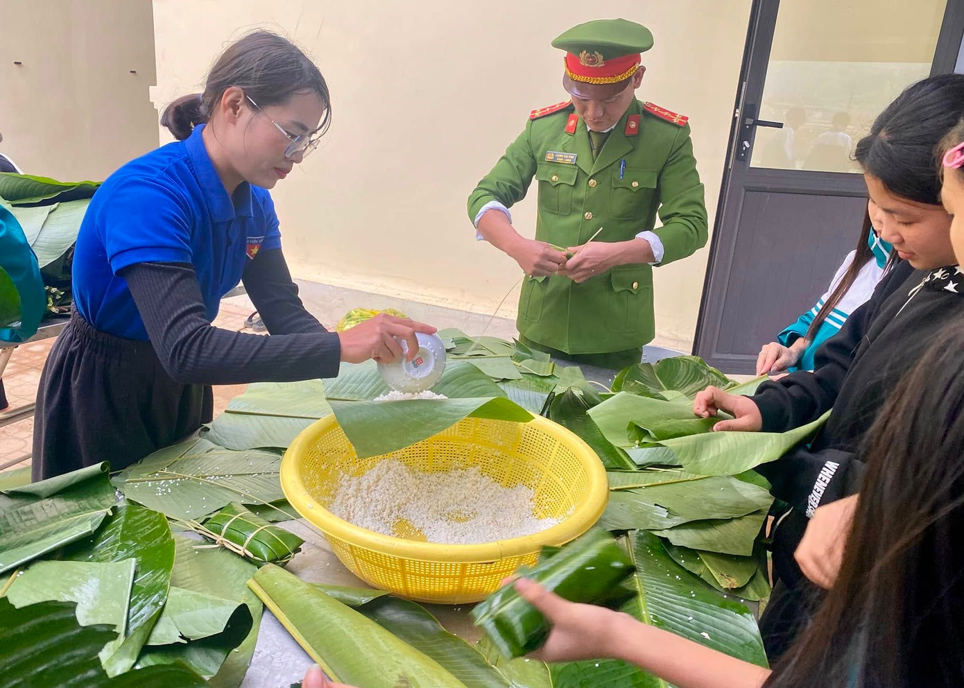 Các đoàn viên, cán bộ công an và các em học sinh cùng nhau gói những chiếc bánh cổ truyền.