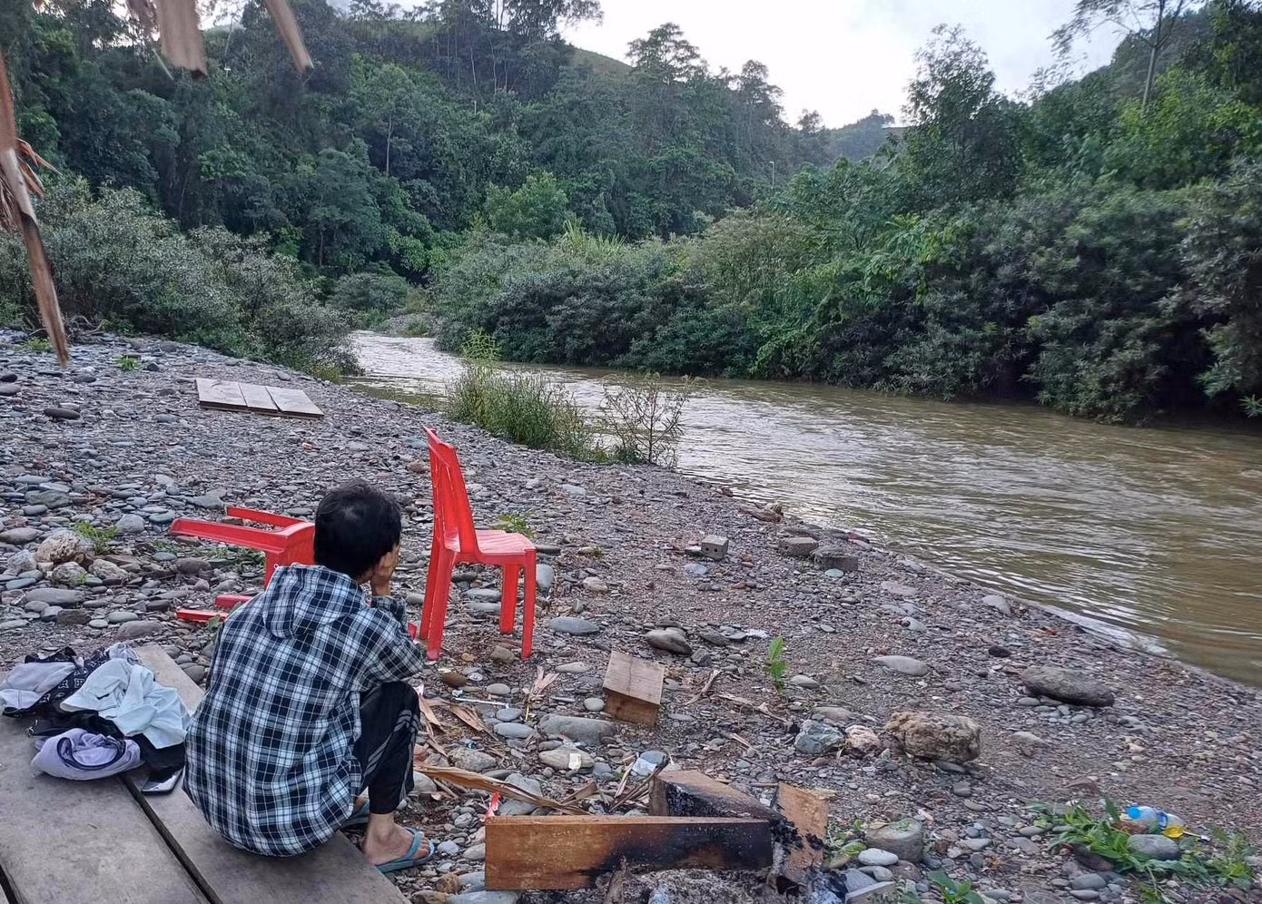 Người thân nam sinh ngồi ngóng đợi tin tức bên dòng suối.