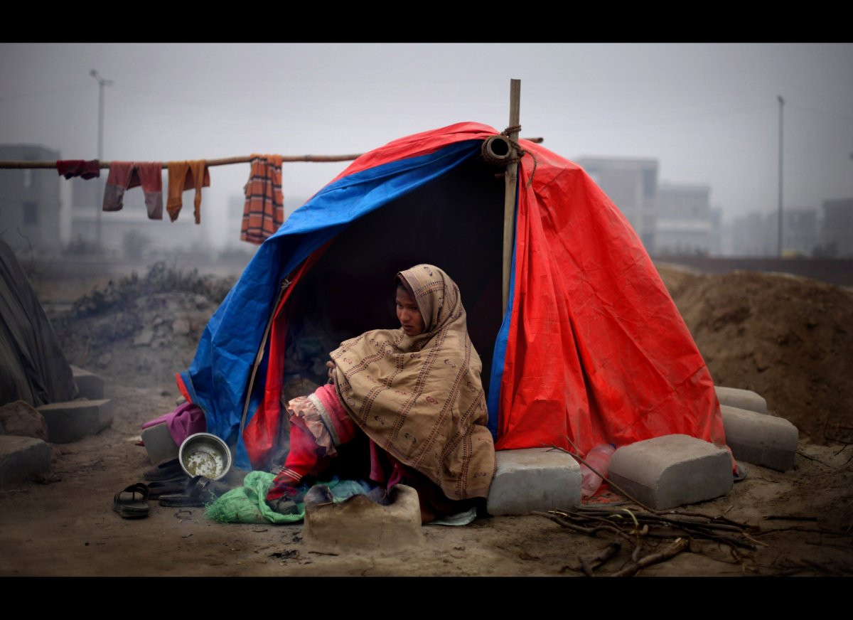 Một phụ nữ Ấn Độ ôm con ngồi trong chiếc lều rách nát để giữ ấm