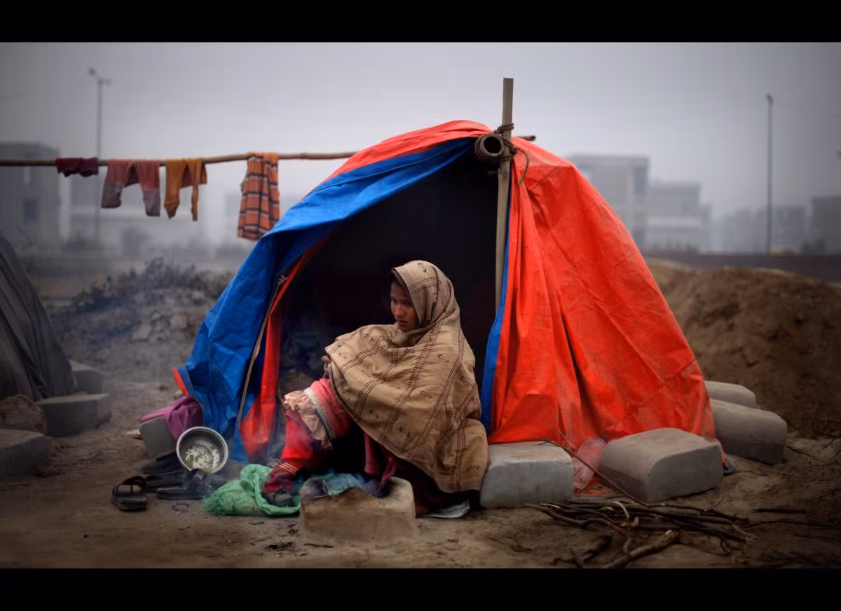 Một phụ nữ Ấn Độ ôm con ngồi trong chiếc lều rách nát để giữ ấm