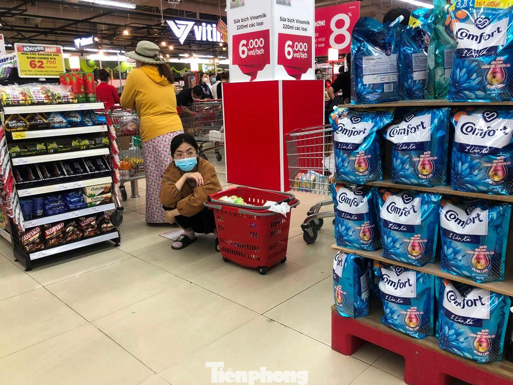 Một khách hàng mệt mỏi ngồi bệt chờ dòng người xếp hàng dài thanh toán