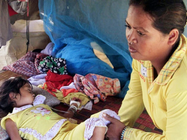 Mean Thida, bốn tuổi, mắc bệnh lạ đang nằm bên mẹ và được truyền huyết thanh tại nhà, gần một bãi rác ở làng Sambour, ngoại ô thủ đô Phnom Penh, Campuchia, hôm 9-7 Ảnh: AP