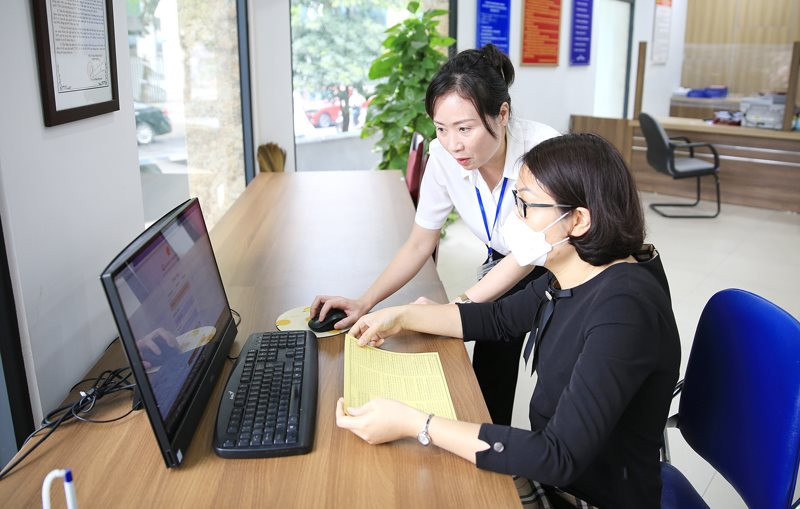 Cán bộ công chức hỗ trợ người dân thực hiện giao dịch trên Cổng dịch vụ công trực tuyến tại bộ phận “một cửa” quận Tây Hồ (Ảnh: Quang Thái)
