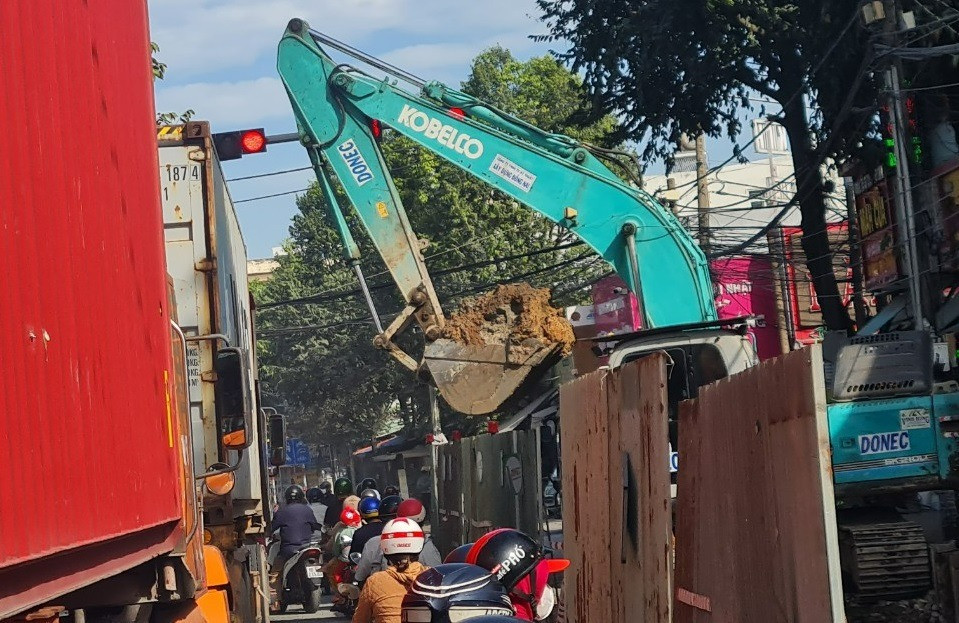 Người đi đường lo sợ khi nhìn thấy chiếc gầu xúc đầy đất lơ lửng ngay trên đầu.