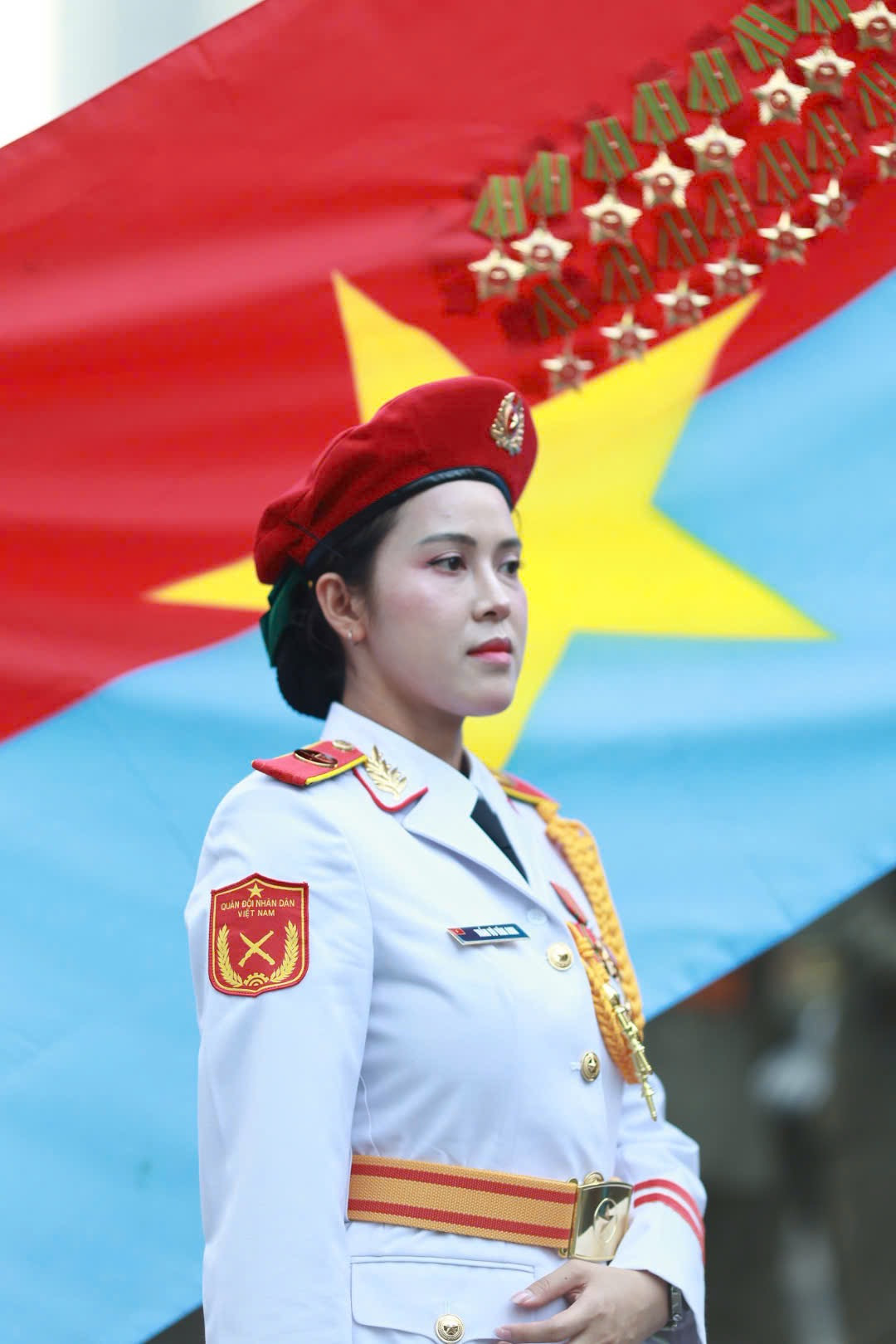 Các nữ chiến sĩ thuộc khối Quân nhạc đứng trang nghiêm trước lá cờ Mặt trận Dân tộc giải phóng miền Nam Việt Nam. Đây là một trong những nữ chiến sĩ đại diện hình ảnh “bông hồng thép” thuộc lực lượng Quân đội Nhân dân Việt Nam.