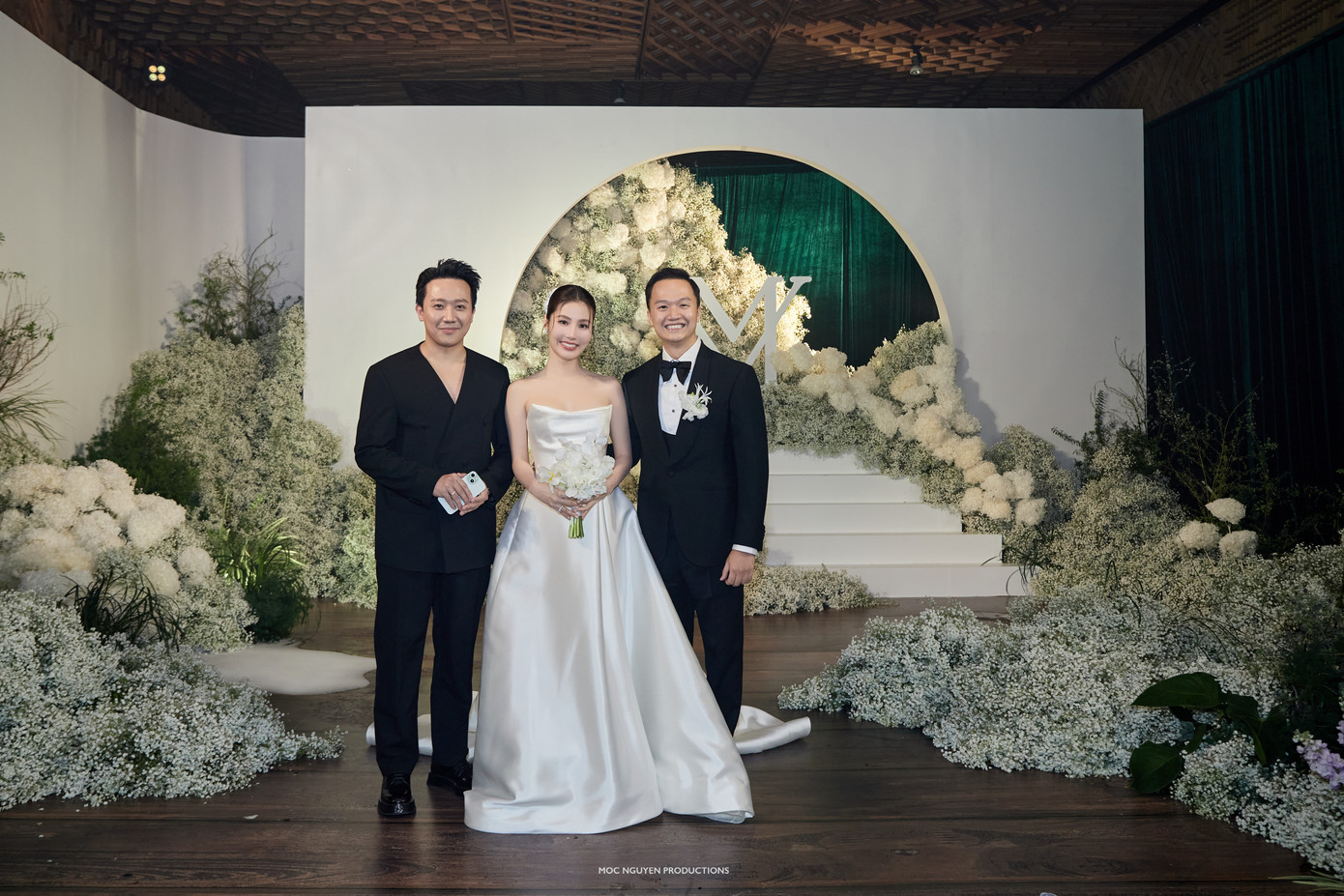 Trấn Thành bên cô dâu chú rể. Tiệc cưới của Diễm My có thiết kế sang trọng, phủ kín hoa tươi màu trắng. Nữ diễn viên và chồng đã dành thời gian dài để chuẩn bị cho ngày vui. Cô bày tỏ bản thân hạnh phúc khi được khoác lên mình chiếc váy cưới.