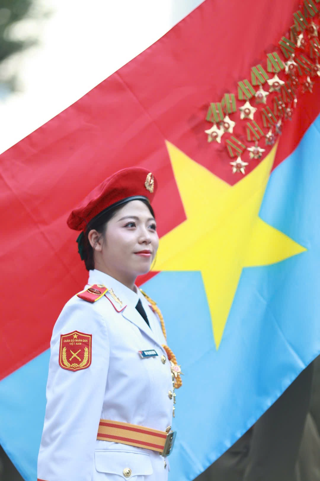 Các nữ chiến sĩ thuộc khối Quân nhạc đứng trang nghiêm trước lá cờ Mặt trận Dân tộc giải phóng miền Nam Việt Nam. Đây là một trong những nữ chiến sĩ đại diện hình ảnh “bông hồng thép” thuộc lực lượng Quân đội Nhân dân Việt Nam.