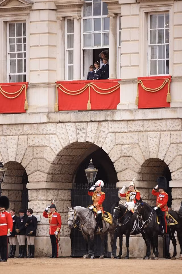 Khoảnh khắc Công nương Kate Middleton và ba người con vẫy tay chào đám đông từ ban công Cung điện Buckingham. Bên dưới là thành viên của Hộ Kỵ binh Hoàng gia Anh vừa hoàn thành nhiệm vụ hộ tống, đảm bảo an toàn cho Nhà vua, Hoàng hậu, gia đình của Thân vương xứ Wales trong cuộc diễu hành.