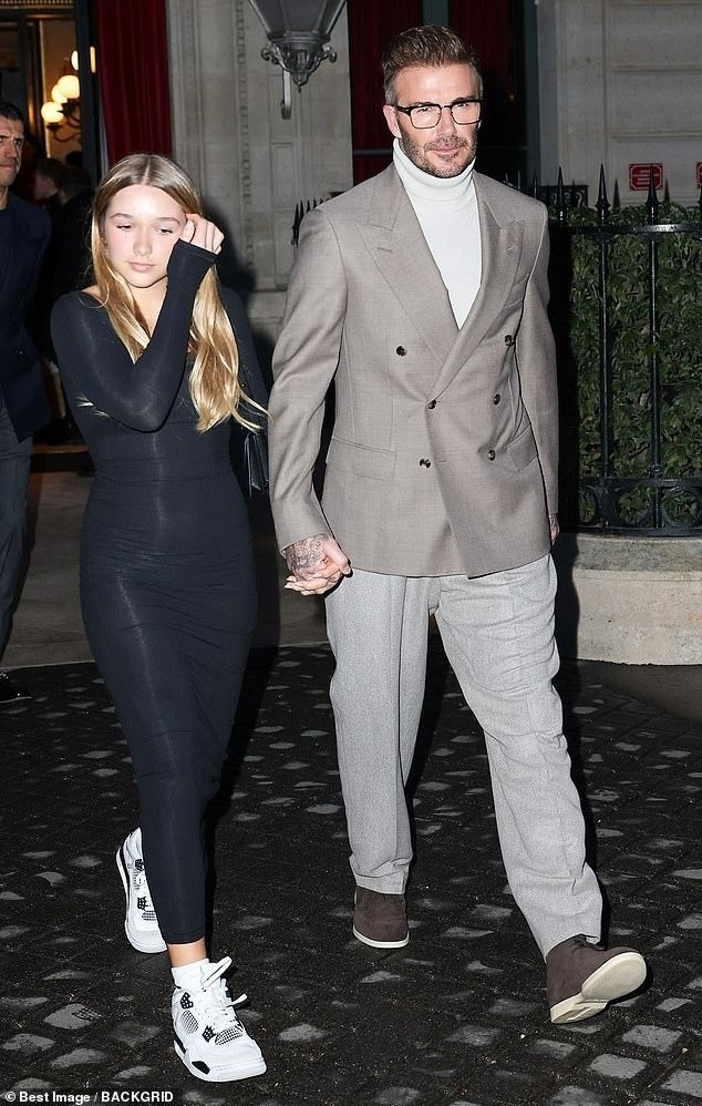 Beckham phối vest xám cùng áo len cổ lọ. Beckham được khen giữ được phong độ ở tuổi 49. Cựu danh thủ người Anh nắm tay con gái dự show thời trang.