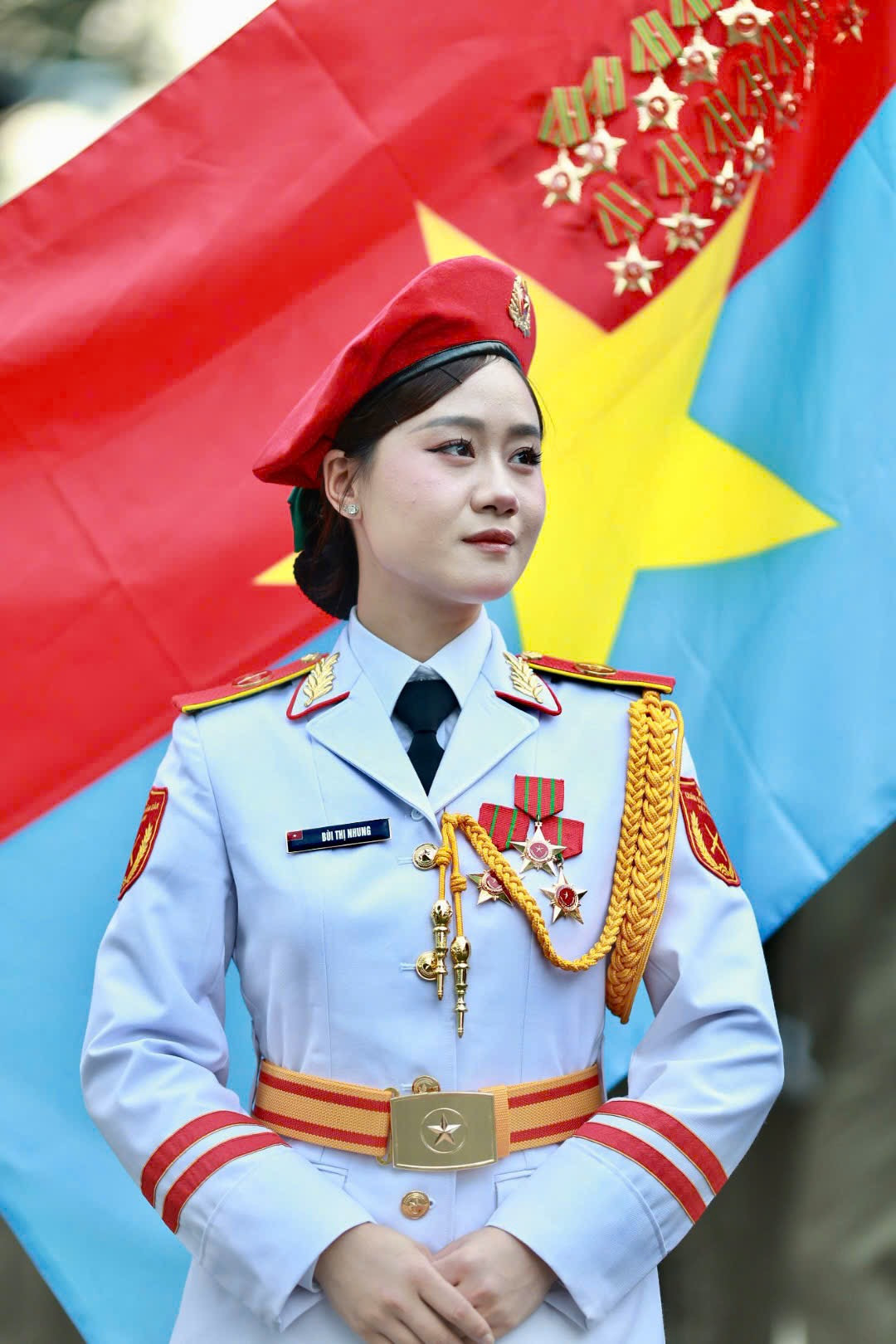 Các nữ chiến sĩ thuộc khối Quân nhạc đứng trang nghiêm trước lá cờ Mặt trận Dân tộc giải phóng miền Nam Việt Nam. Đây là một trong những nữ chiến sĩ đại diện hình ảnh “bông hồng thép” thuộc lực lượng Quân đội Nhân dân Việt Nam.