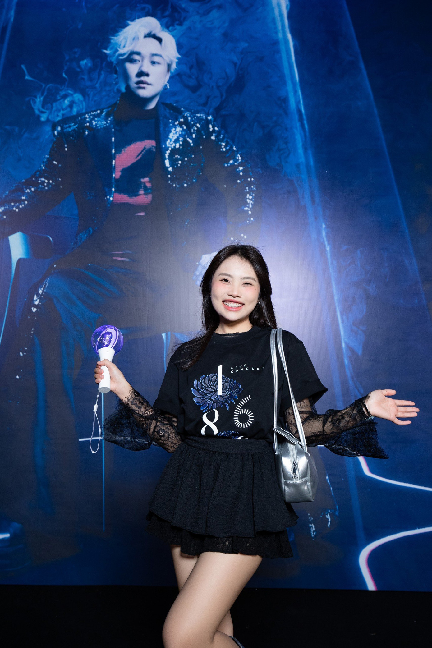 Phương Mỹ Chi trang điểm đậm phong cách Gen Z trong đêm nhạc tối 13/7. Cô diện áo của ban tổ chức, dùng lightstick để ủng hộ đồng nghiệp. Nữ ca sĩ tạo điểm nhấn khi phối trang phục ren bên trong cùng áo phông in họa tiết.