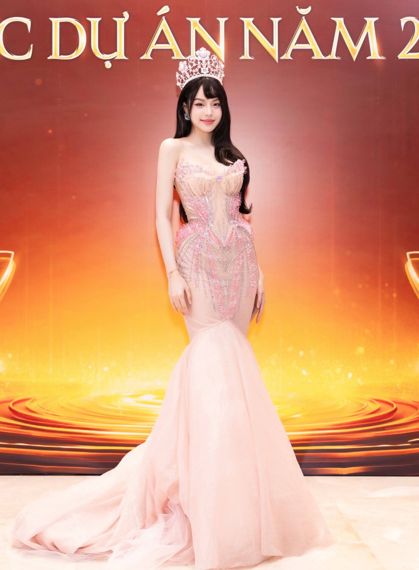 Xuất hiện tại thảm đỏ quy tụ dàn hoa hậu, á hậu đình đám chiều 26/3 tại TPHCM, Hoa hậu Huỳnh Thị Thanh Thủy gây ấn tượng với chiếc đầm hồng pastel dáng đuôi cá được đính kết cầu kỳ. Họa tiết pha lê nổi bật phần eo và ngực, tôn lên đường cong gợi cảm. Đương kim Hoa hậu Việt Nam - Hoa hậu Quốc tế kết hợp layout makeup nhẹ nhàng với kiểu tóc xõa đơn giản.