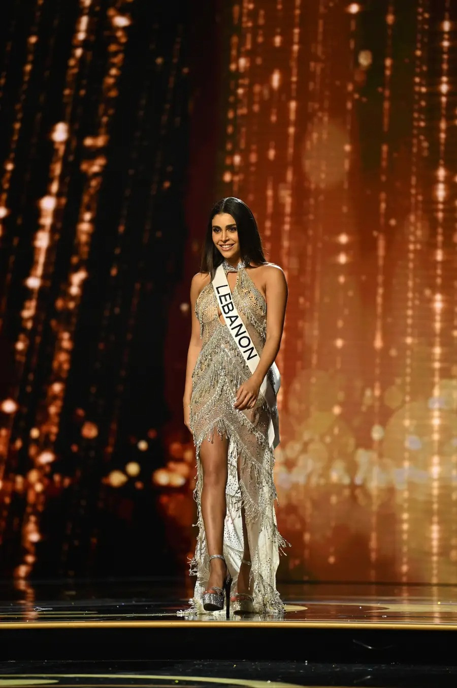 Bộ trang phục với loạt tua rua 3D làm tôn lên vẻ ngoài vừa gợi cảm lại thanh lịch của người đẹp Lebanon. Những chi tiết xuyên thấu, phần xẻ tà cao ở giữa giúp Yasmina Zaytoun nổi bật trên sân khấu.