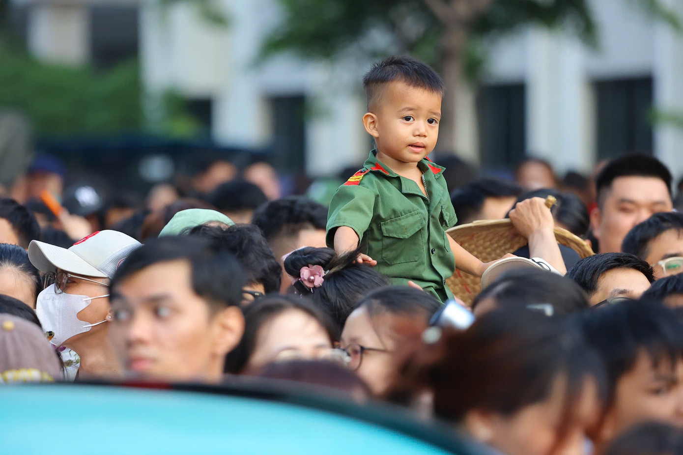 Những em bé được bố mẹ cõng trên lưng, hòa vào không khí đông đúc và đầy tự hào giữa biển người khu vực đường Lê Duẩn, hướng ra trục Lê Lợi - Nam Kỳ Khởi Nghĩa.