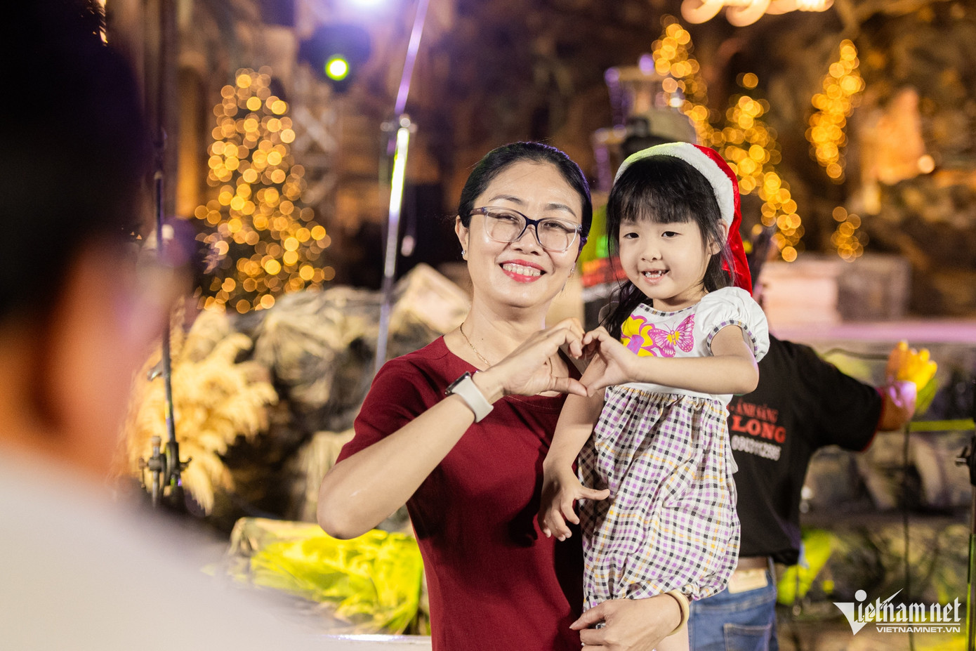 Em nhỏ tạo dáng tinh nghịch cùng bà phía trước tiểu cảnh hang đá rực rỡ.