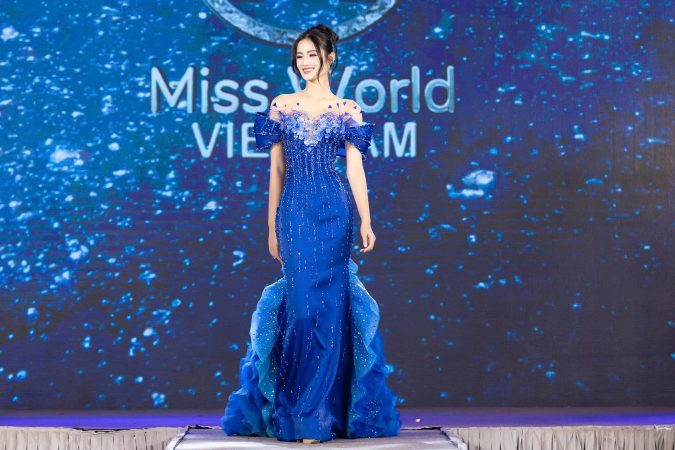 Thiết kế trễ vai gợi cảm, chi tiết đính kết 3D cầu kỳ giúp cô tôn dáng và sang trọng. Phần tà váy được NTK Hoàng Tony xử lý xếp tầng mềm mại, gợn sóng uyển chuyển, mang lại hiệu ứng thị giác ấn tượng. Cô chuẩn bị kỹ lưỡng từ trang phục, tiết mục trình diễn... để thể hiện thân tại Miss World lần thứ 72 diễn ra tại Telangana, Ấn Độ từ ngày 7/5.