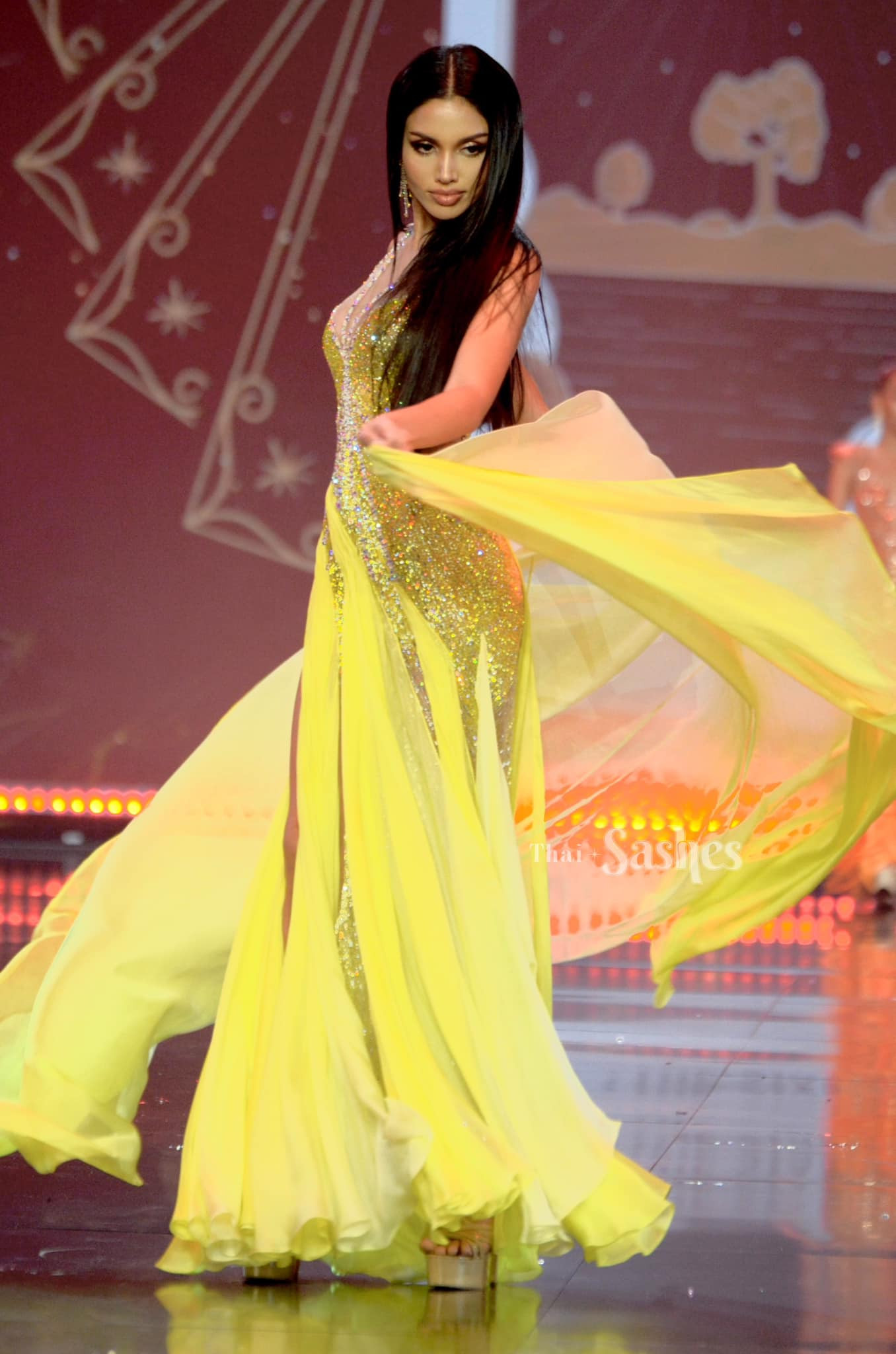 Người đẹp Veena Praveenar Singh (Á hậu 1 Hoa hậu Hoàn vũ Thái Lan 2020) chọn tông màu vàng cho phần trình diễn váy dạ hội. Phần tà váy phía sau giúp cô bay bổng hơn khi catwalk. Veena có kỹ năng trình diễn ấn tượng, chuyên nghiệp.