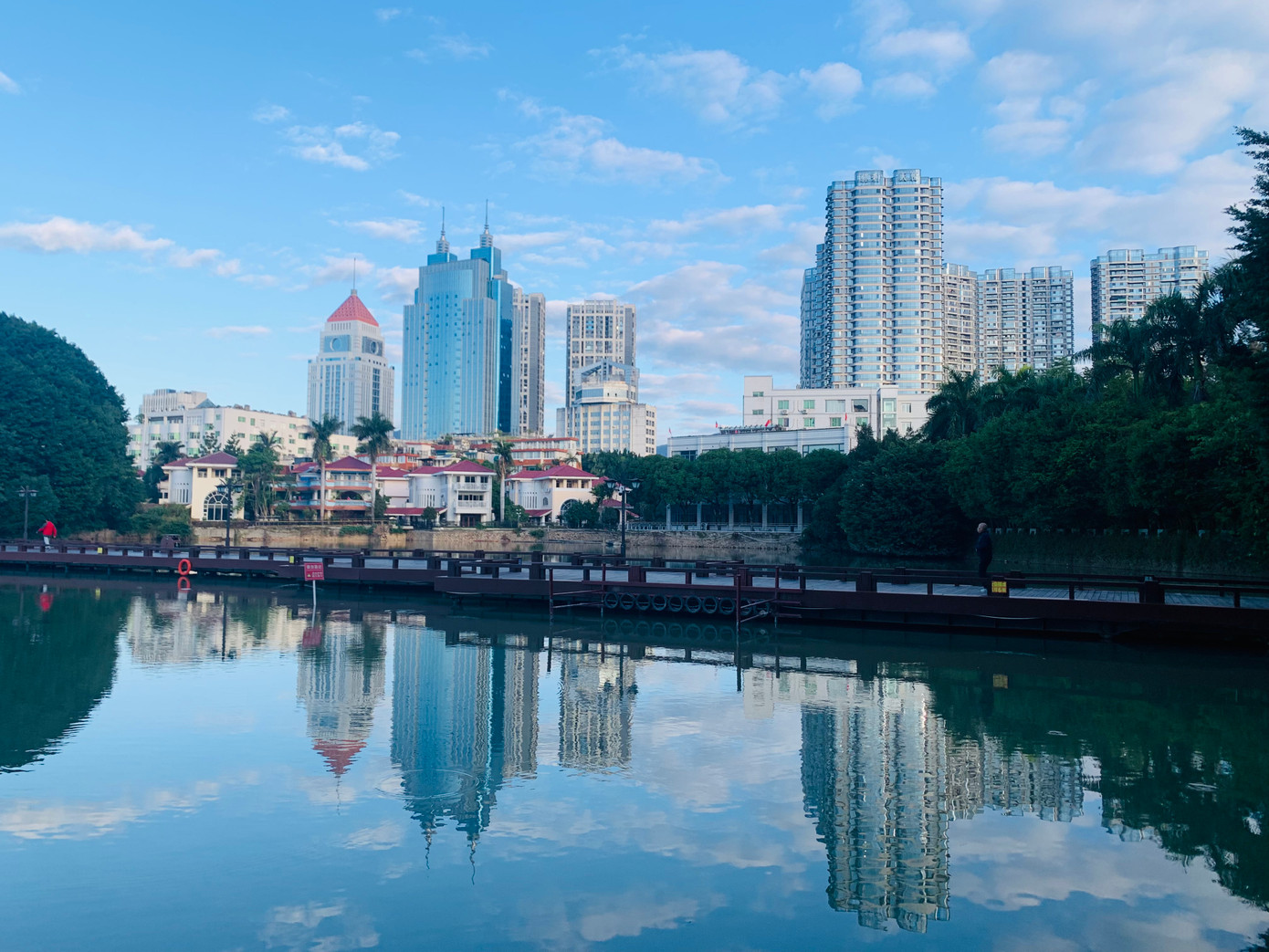 Hồ Tây ở Phúc Châu, Phúc Kiến có nhiều loài cây to nhỏ khác nhau, từ cổ thụ với gốc rễ xù xì tới dây leo ngoằn ngoèo, hoa tím, hoa đỏ, hoa vàng… Ven hồ, các tòa nhà cao tầng soi bóng nước lung linh. Ảnh: Linh Nhi.