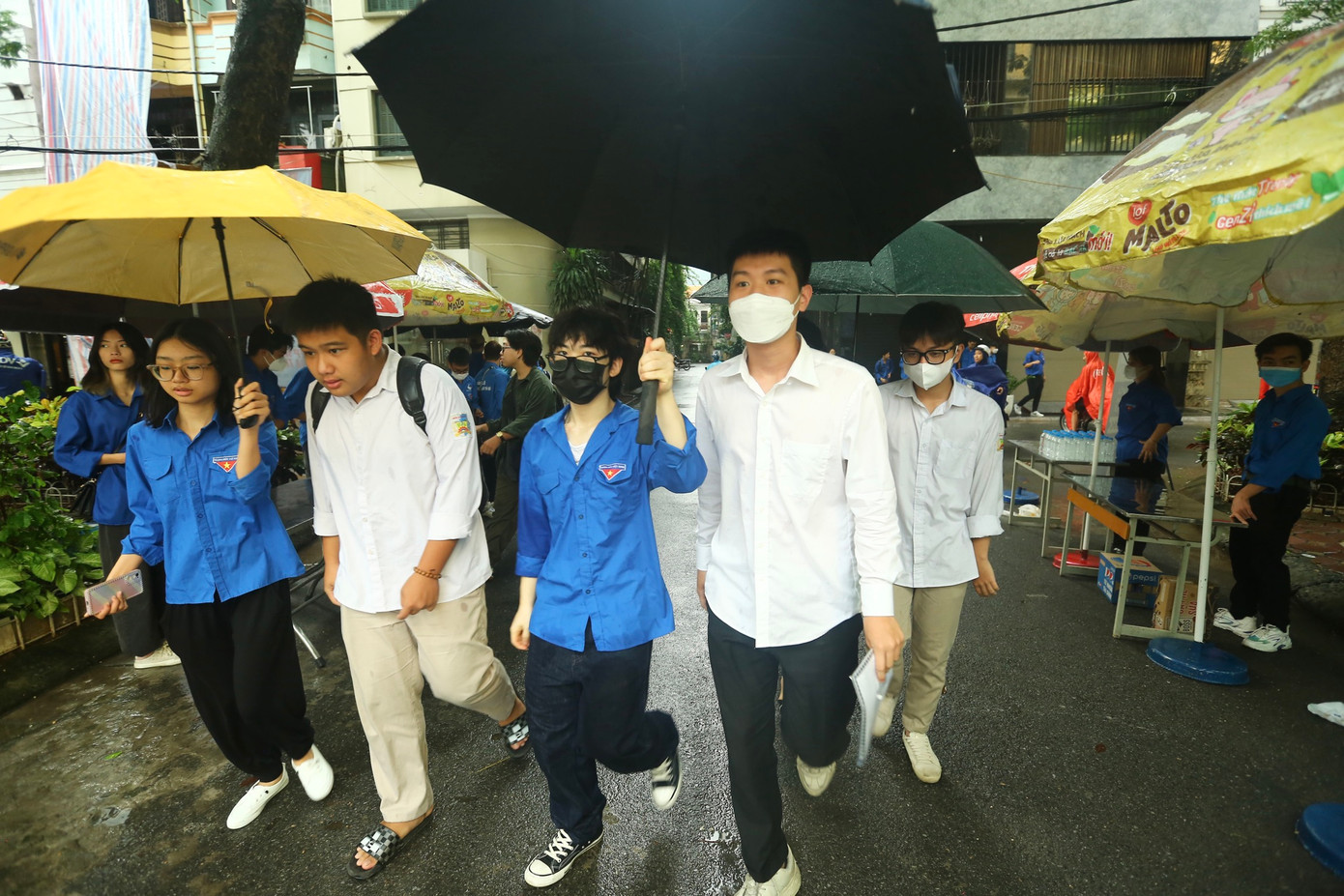 Ghi nhận tại điểm trường THPT Phan Huy Chú (Đống Đa, Hà Nội), hàng chục &quot;áo xanh&quot; tình nguyện có mặt tại khu vực điểm thi này, đội mưa, che ô cho các thí sinh trong buổi thi đầu tiên.