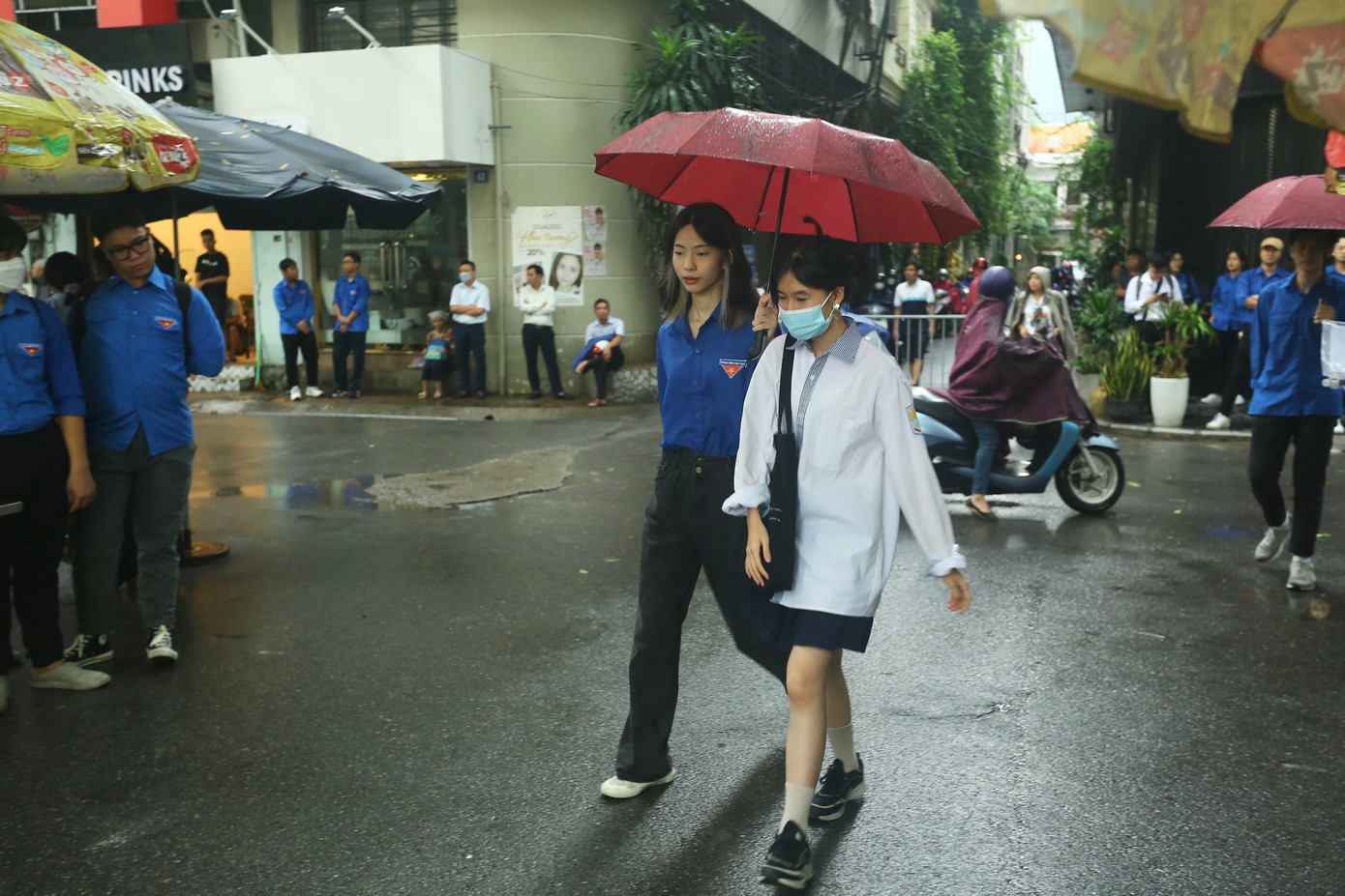 Áo xanh tình nguyện đội mưa che ô cho thí sinh từ cổng vào đến phòng thi trước giờ tập trung.