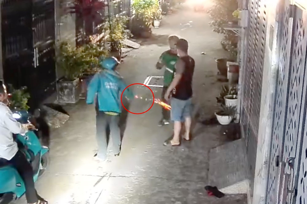 Tài xế xe ôm công nghệ vứt pháo nổ (khoanh tròn đỏ) vào chỗ anh L. đang đứng. Ảnh cắt từ clip. Tài xế xe ôm công nghệ vứt pháo nổ (khoanh tròn đỏ) vào chỗ anh L. đang đứng. Ảnh cắt từ clip.