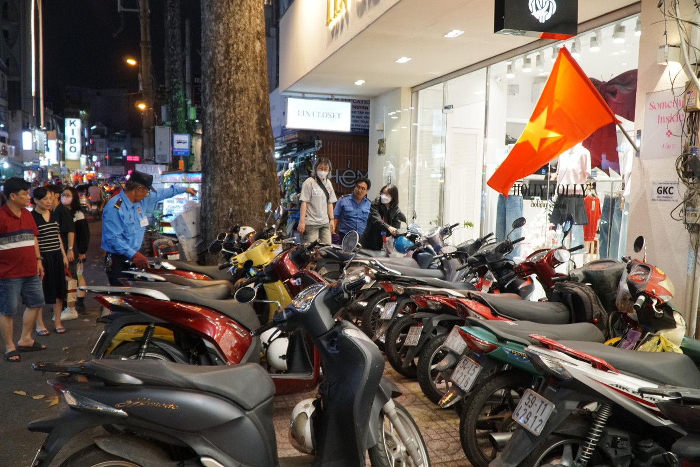 Nhân viên bảo vệ một cửa hàng quần áo nữ liên tục dắt xe ra, vào và ghi vé cho khách.