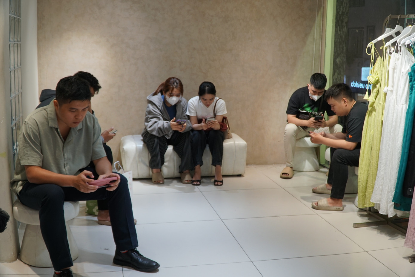 Bên trong một cửa hàng thời trang, hơn chục bạn trẻ đang xếp hàng chờ thử đồ. Một số người ngồi lướt điện thoại trong lúc chờ người thân thử quần áo.