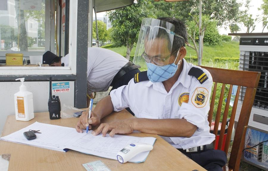 Bảo vệ tòa nhà kiểm soát chặt chẽ người đến giao hàng bằng cách kiểm tra giấy tờ tùy thân, ghi lại thông tin cá nhân, đo thân nhiệt. (Ảnh: Thu Ngà)