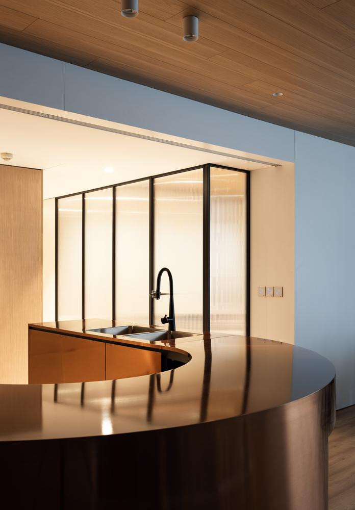 Lối vào chính của căn hộ được chắn bởi quầy bar (đồng thời là đảo bếp) được làm từ đồng nguyên khối chải xước. Với thiết kế độc đáo và chất liệu sáng bóng, quầy bar trở thành điểm nhấn của căn hộ.