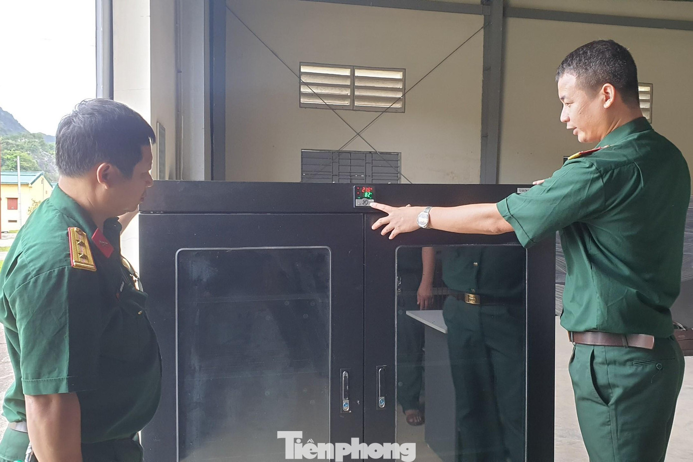 Thiếu tá Lê Anh Tuấn (bên phải) trao đổi với đồng đội về tính năng của tủ bảo quản khí tài quang học chuyên ngành biên phòng