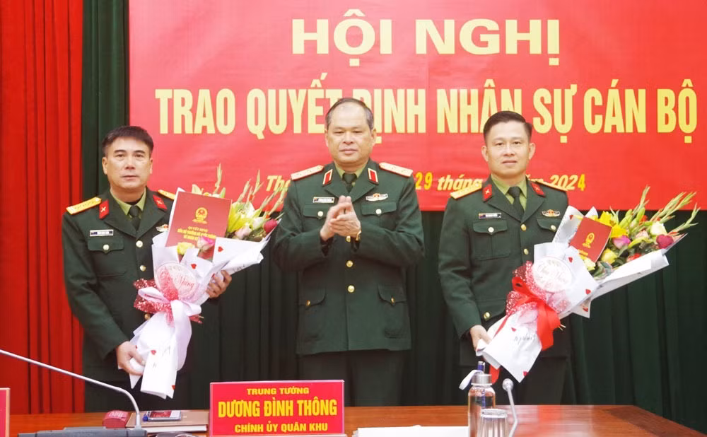 Trung tướng Dương Đình Thông, Bí thư Đảng ủy, Chính ủy Quân khu 1, trao quyết định bổ nhiệm chức vụ và tặng hoa chúc mừng Đại tá Trần Ngọc Tiến (bên trái), Thượng tá Ân Trung Tuyến. Ảnh: Chinhphu.vn.